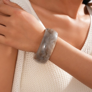 Close-up of a wide acrylic resin bangle featuring grey marble texture on a female wrist