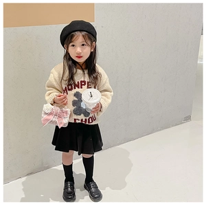Toddler girl in beige bear sweater and black pleated skirt with pink bow handbag