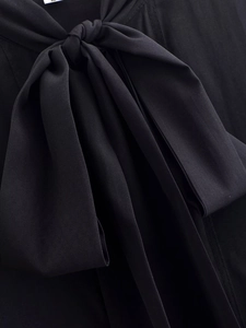 Close-up of the elegant large bow detail on the neckline of a black long-sleeve blouse