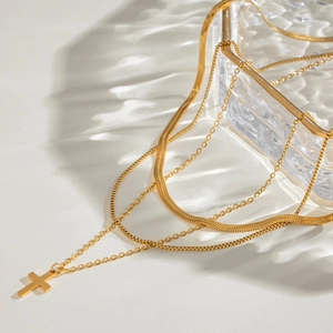 Layered gold stainless steel necklace set with snake chain and cross pendant on white surface