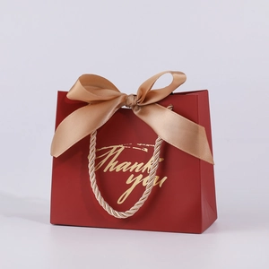 Close-up of red gift bag with gold ribbon bow, woven handle and gold Thank You text