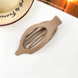 Detail view of a large brown matte hair claw clip on a white table with a coffee cup