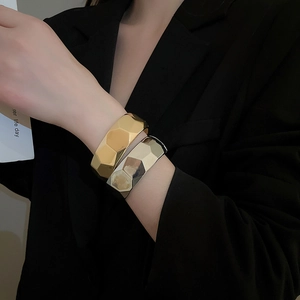 Detail of geometric faceted gold and silver wide cuffs worn on a black blazer sleeve