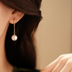 Close-up of gold-plated drop earring with zircon studs and white pearl pendant