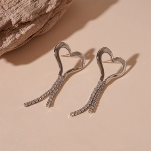 Detail of silver heart tassel earrings with sparkling rhinestones on a natural stone surface