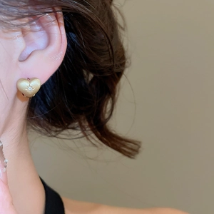 Close-up of a gold heart-shaped zircon earring with a brushed texture on a model