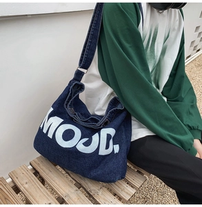 Detail of blue denim crossbody bag with white MOOD lettering shown on a model