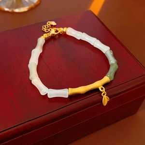 Close-up of bamboo-style jade bracelet with green beads and leaf pendant on wood