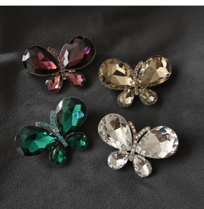 Macro shot of colorful crystal butterfly brooches in emerald, red, and gold set on velvet