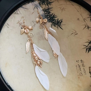 Detail of bohemian long feather earrings with gold chains and peace sign charms