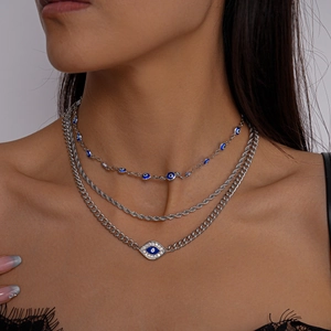 Close-up of triple-layered silver necklace featuring blue evil eye charms and rhinestone accents