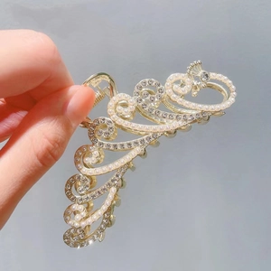 Detail of golden peacock hair claw clip with sparkling rhinestones and white pearls