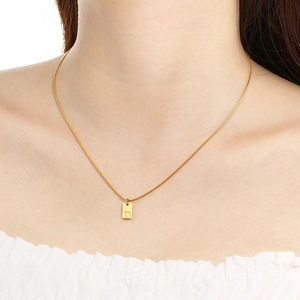 Close-up of golden necklace featuring a small rectangular tag with engraved letter D