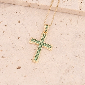 Dettaglio del ciondolo a croce in oro 18K con pietre verdi su base in pietra