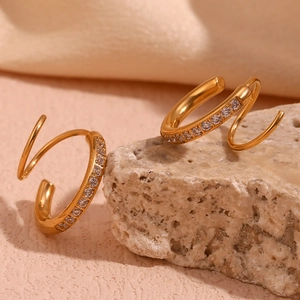 Détail des boucles d'oreilles spirales dorées avec zircons sur fond de pierre naturelle