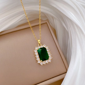 Macro shot of gold necklace with emerald rectangle pendant and zircon halo on silk fabric