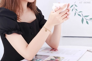 Detail shot of a minimalist gold padlock charm bracelet worn by a model holding a cup