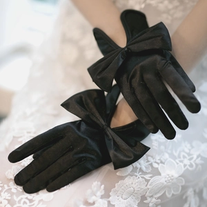 Detail of black satin short bridal gloves with elegant bow on white lace background