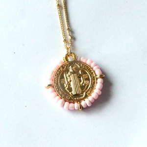 Macro detail of gold Virgin Mary pendant with pink bead trim and engraved religious relief