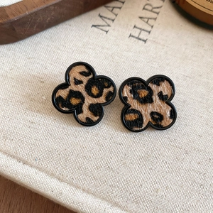 Detailed close-up of leopard print clover earrings on a textured beige linen background