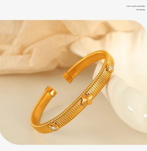 Detail of gold four-leaf clover bracelet with embedded zircons on a white ceramic plate