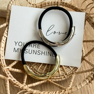 Close-up of minimalist hair ties with gold and silver crescent metal charms on a card