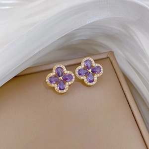 Close-up of gold clover earrings with purple pear-cut stones and pave zircon accents