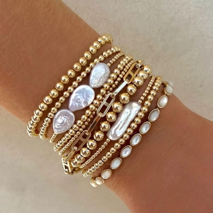 Detail view of layered 18K gold-plated bracelets featuring baroque pearls and metal links