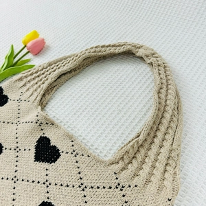 Flat lay of beige knitted tote bag with black heart and diamond patterns with tulips