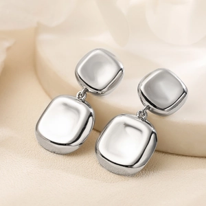 Minimalist silver geometric square earrings on beige fabric with white pedestal