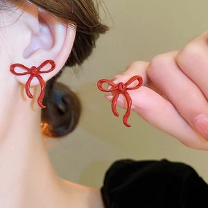 Close-up of red bow-shaped stud earrings showing worn size and smooth lacquered finish