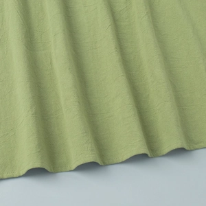 Close-up of avocado green cotton fabric texture and delicate sewing on the dress hem