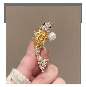 Macro detail of golden koi fish brooch with clear rhinestones and a white pearl accent