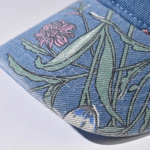 Detailed close-up of blue denim baseball cap brim featuring green leaf and floral prints