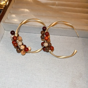Close-up of matte gold C-shaped twisted earrings with hand-wrapped sandalwood beads