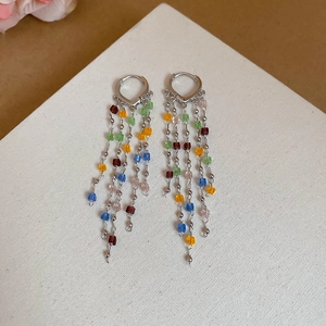 Detail of colorful crystal fringe heart earrings with silver chains on white fabric