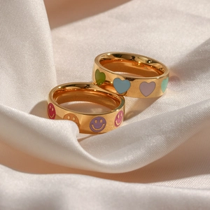 Close-up of gold stainless steel rings with colorful smiley face and heart oil drip patterns