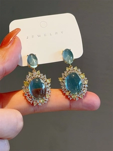 Close-up of gold earrings with mint blue cat eye stones and surrounding zircons