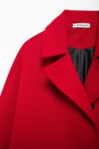 Detail view of the red wool coat lapel with a white brand size label and black lining