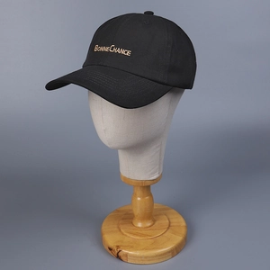 Close-up of golden Bonne Chance embroidery on a black cotton twill baseball cap detail