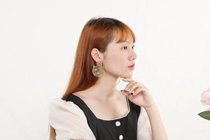 Close-up of a gold clover flower earring worn by a model against a white background