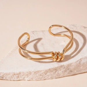 Detail of gold double-layer geometric knotted cuff bracelet on white stone