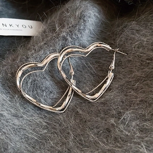 Detail of silver double-layered heart hoop earrings with textured inner ring on plush