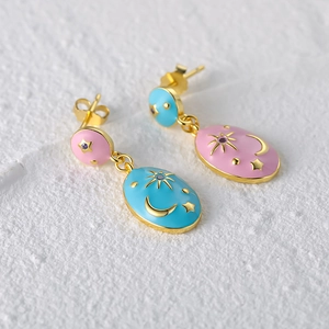 Macro shot of asymmetric gold-tone enamel earrings with celestial sun moon and star motifs