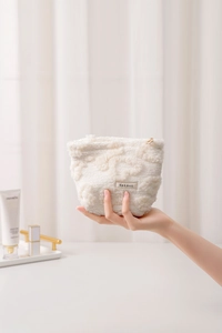 Detail of cream plush makeup bag featuring 3D floral texture and gold zipper closure