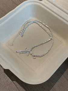 Detail of silver bow necklace with pink heart and pearl in a rustic display box