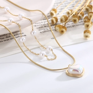 Detail of a double-layered gold necklace with heart pendant and white pearls