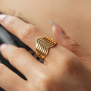 Close-up of a gold hollow geometric ring with leaf-like patterns on a hand