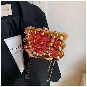Detail of red-orange gradient acrylic clutch with golden metal spheres and chain
