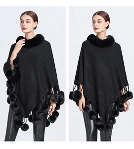 Detail view of black knit poncho featuring faux fur collar and decorative pom-poms
